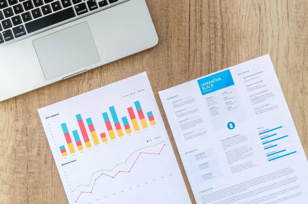 مكتب يتضمن جهاز لابتوب ومجموعة من أوراق تتضمن بيانات تحليل المنافسين - A desk containing a laptop and a set of papers containing competitor analysis data